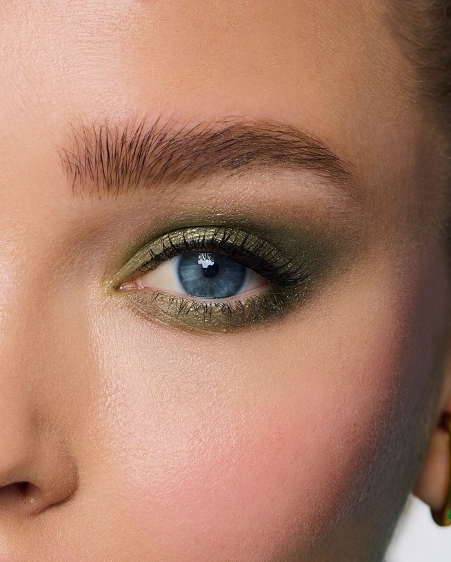 Portrait d'une jeune femme avec un maquillage audacieux : sourcils rose pastel, mascara bleu électrique et lèvres rouge brillant, le tout rehaussé par une tenue violet métallique.
