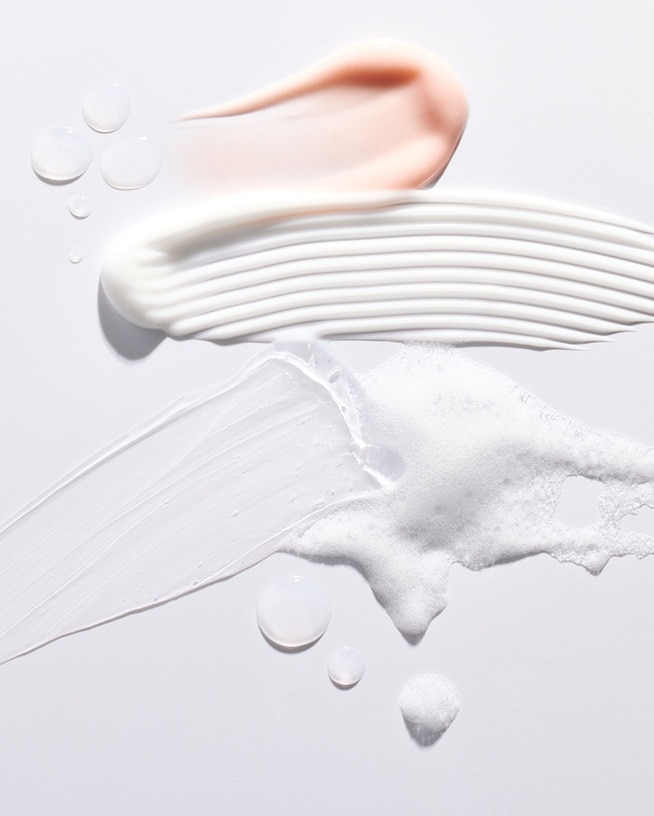 Gros plan sur des échantillons de produits de beauté : une touche rose pêche, une crème blanche striée, un gel transparent et une mousse légère, offrant un aperçu des textures et des formules.