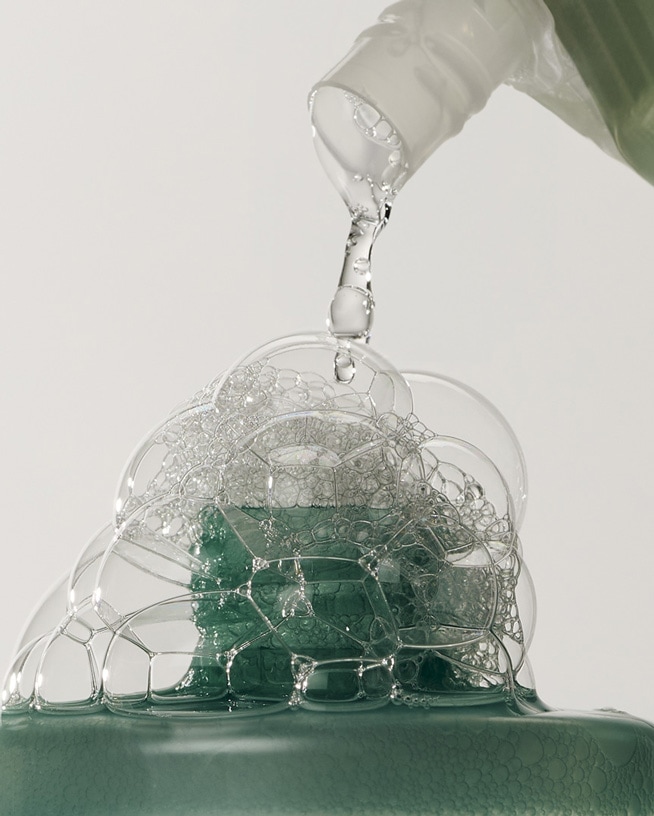 Gros plan sur un liquide vert mousseux versé d'une bouteille, créant une abondance de bulles claires et brillantes.